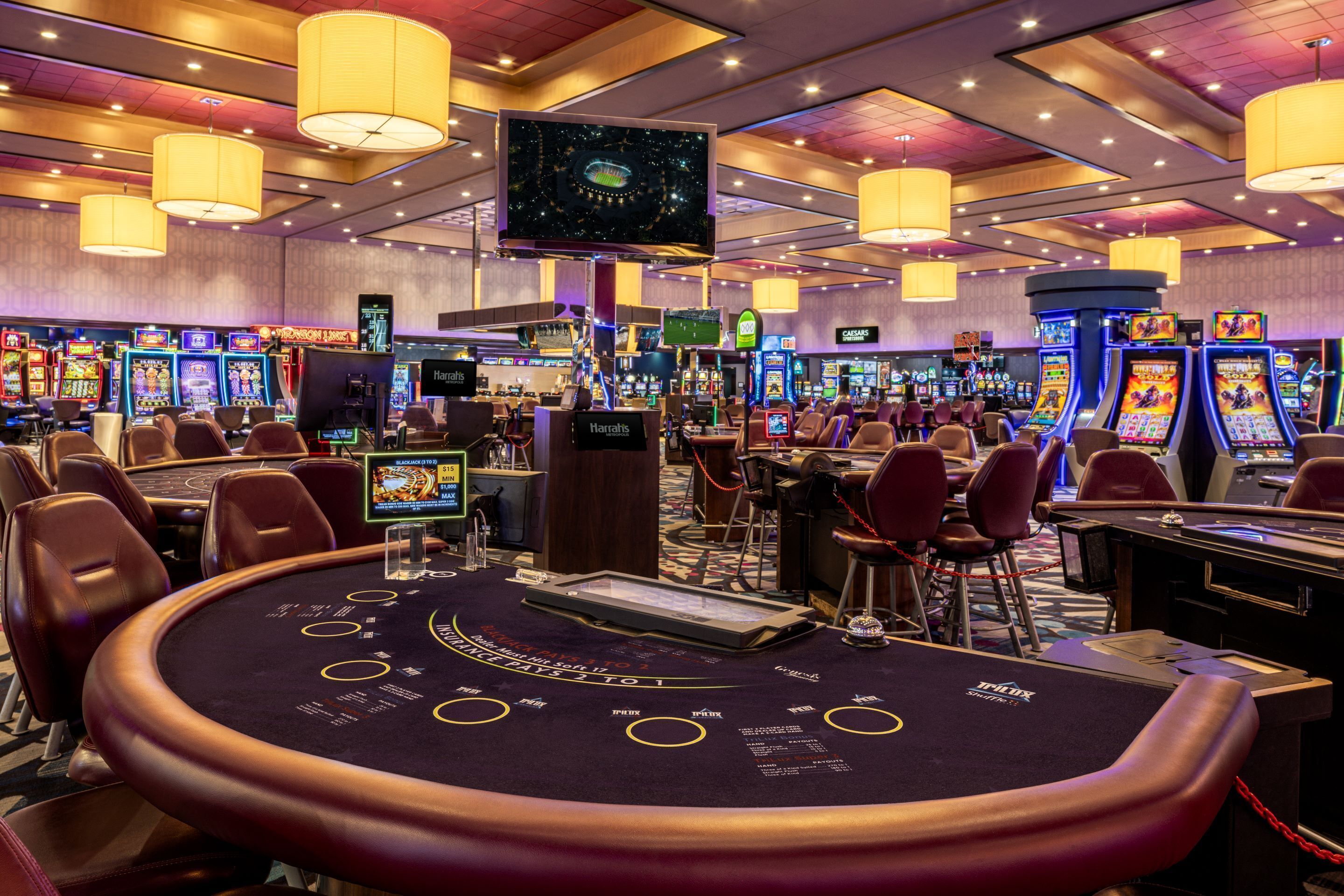A casino with multiple gaming tables, slot machines, and a large screen displaying a game.
