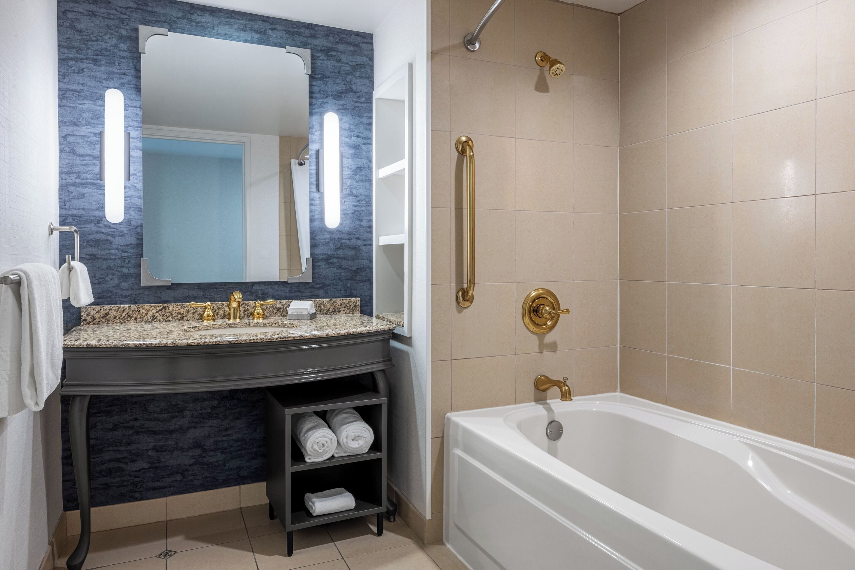 A modern bathroom with a granite countertop, a large mirror, a bathtub, and a shower area.