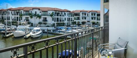 A balcony with a view of a marina, boats, and a building with balconies and palm trees.