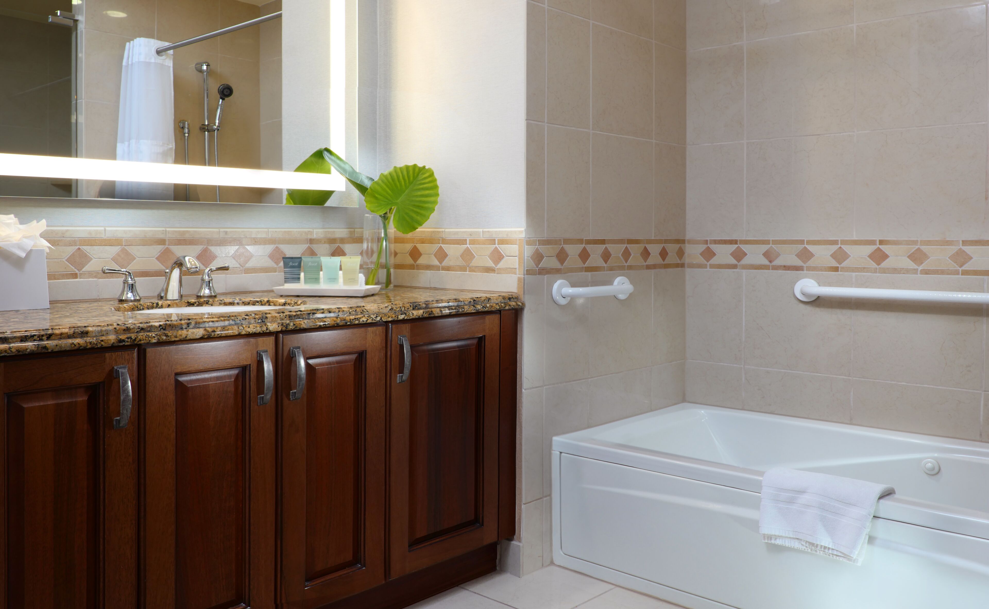 A bathroom with a granite countertop, wooden cabinets, a white bathtub, and a shower area.