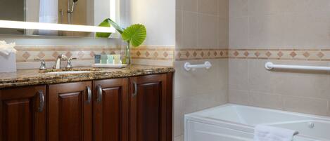 A bathroom with a granite countertop, wooden cabinets, a white bathtub, and a shower area.