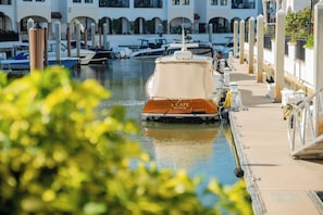 A marina with boats docked, a covered boat named "S Cape" in the foreground, and a building with arches in the background.