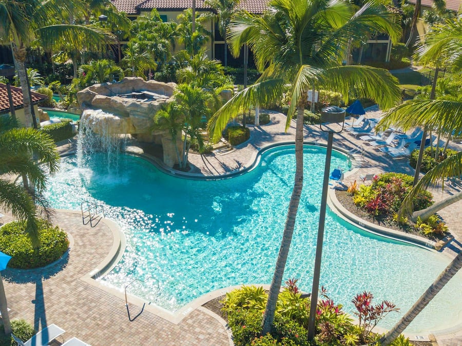 Piscina de resort con cascada, rodeada de palmeras y sillones de descanso.