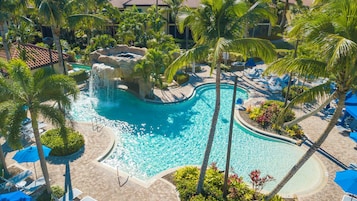 A resort pool with a waterfall feature surrounded by palm trees and lounge chairs.