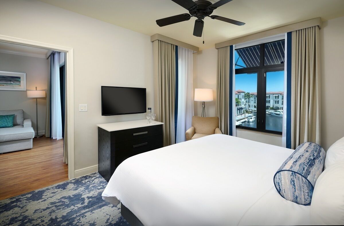 Une chambre d’hôtel équipée d’un lit, d’une télévision, d’un bureau, d’une chaise et d’une fenêtre donnant sur des immeubles.