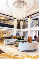 A spacious lobby with a grand chandelier, a reception desk, and a seating area with a coffee table.
