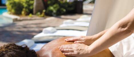 Une personne reçoit un massage du dos sur une table de massage blanche, au bord d’une piscine.