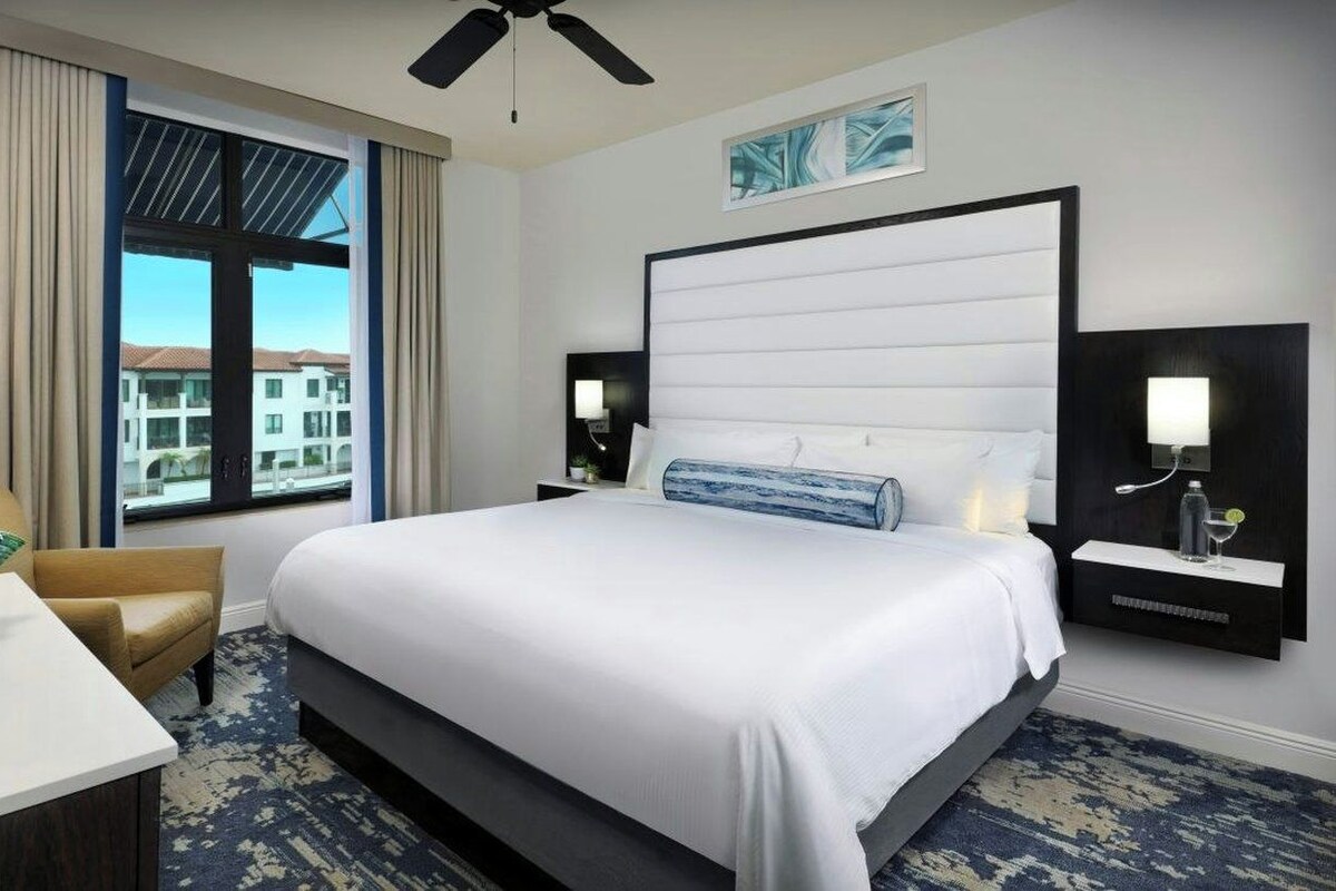 A hotel room with a large bed, a desk, a chair, a window with a view, and a ceiling fan.