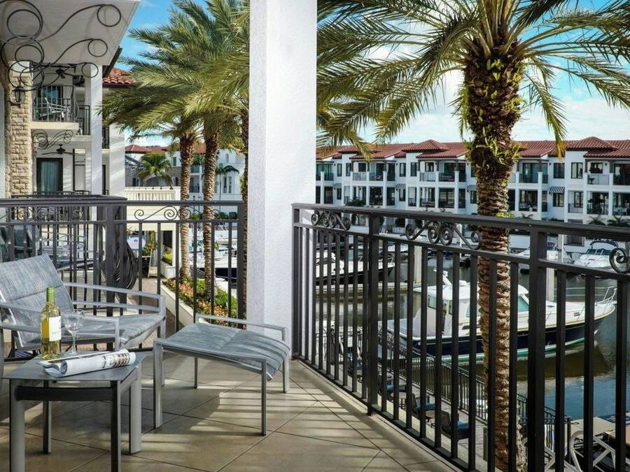 A balcony with a view of a marina, palm trees, and a building with balconies.