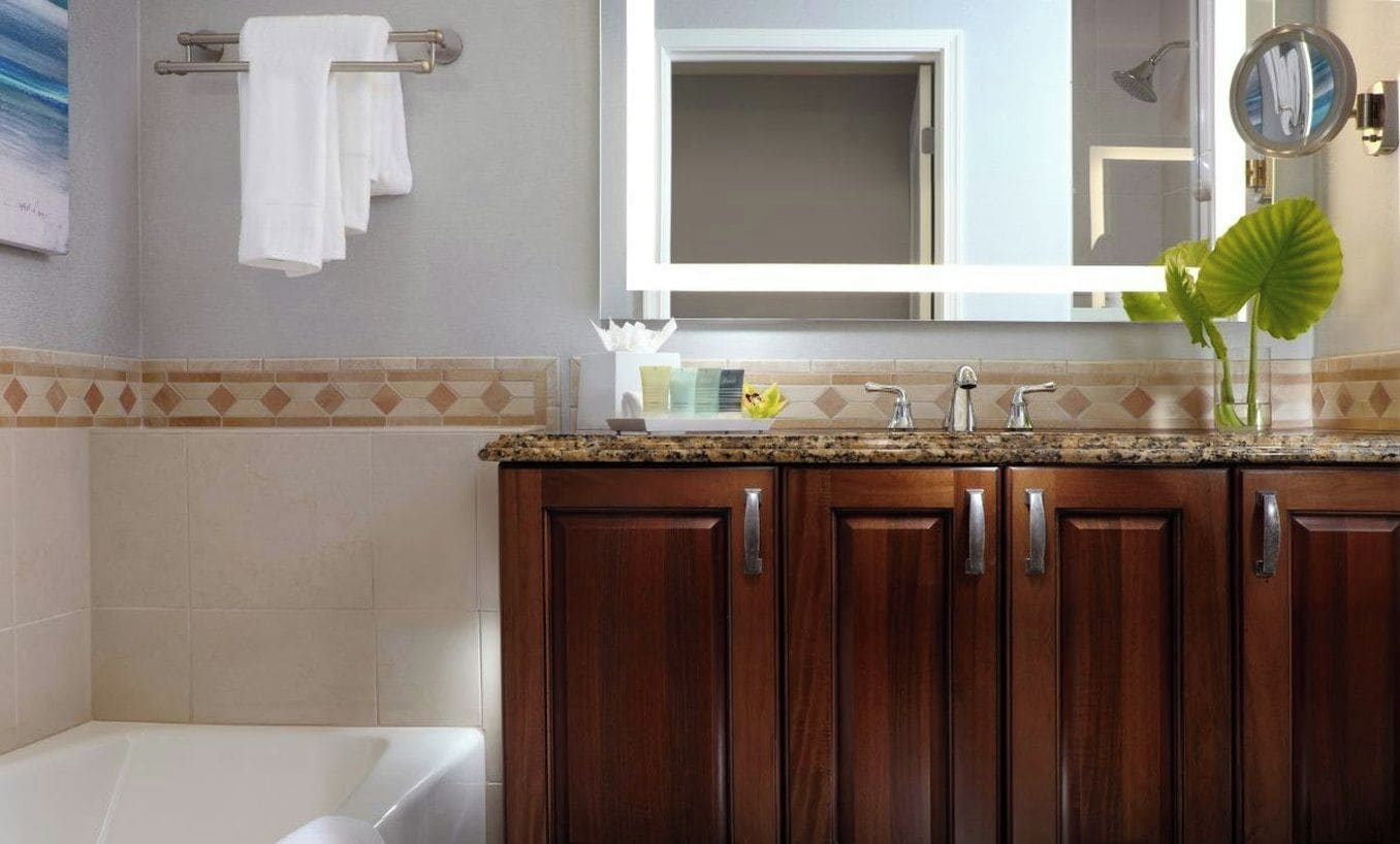 A bathroom with a bathtub, wooden cabinets, a granite countertop, a mirror, and a potted plant.