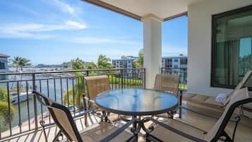 A balcony with a round table and chairs, overlooking a marina and buildings.