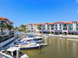 Marina com vários barcos atracados, um edifício à beira-mar com varandas e um céu azul claro.