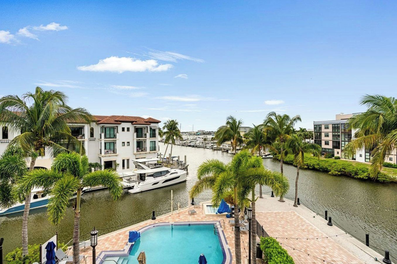 A waterfront property with a swimming pool, a marina with boats, and modern buildings.