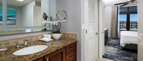A hotel bathroom with a granite countertop, two sinks, a large mirror, and a potted orchid.