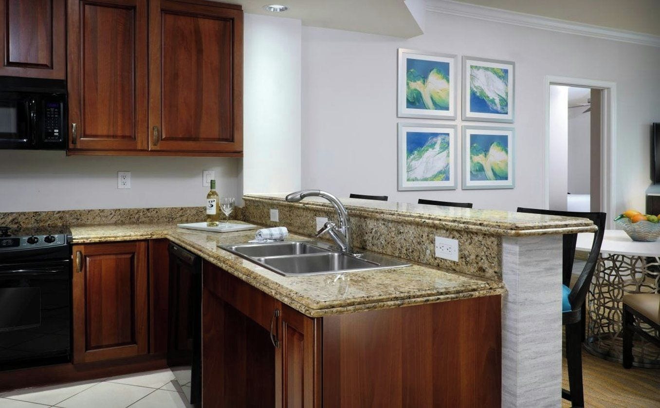 A kitchen with granite countertops, wooden cabinets, a stainless steel sink, and a microwave.