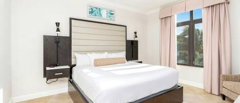 Un dormitorio con una cama grande, un ventilador de techo, una mesita de noche, un televisor montado en la pared y una ventana con cortinas.