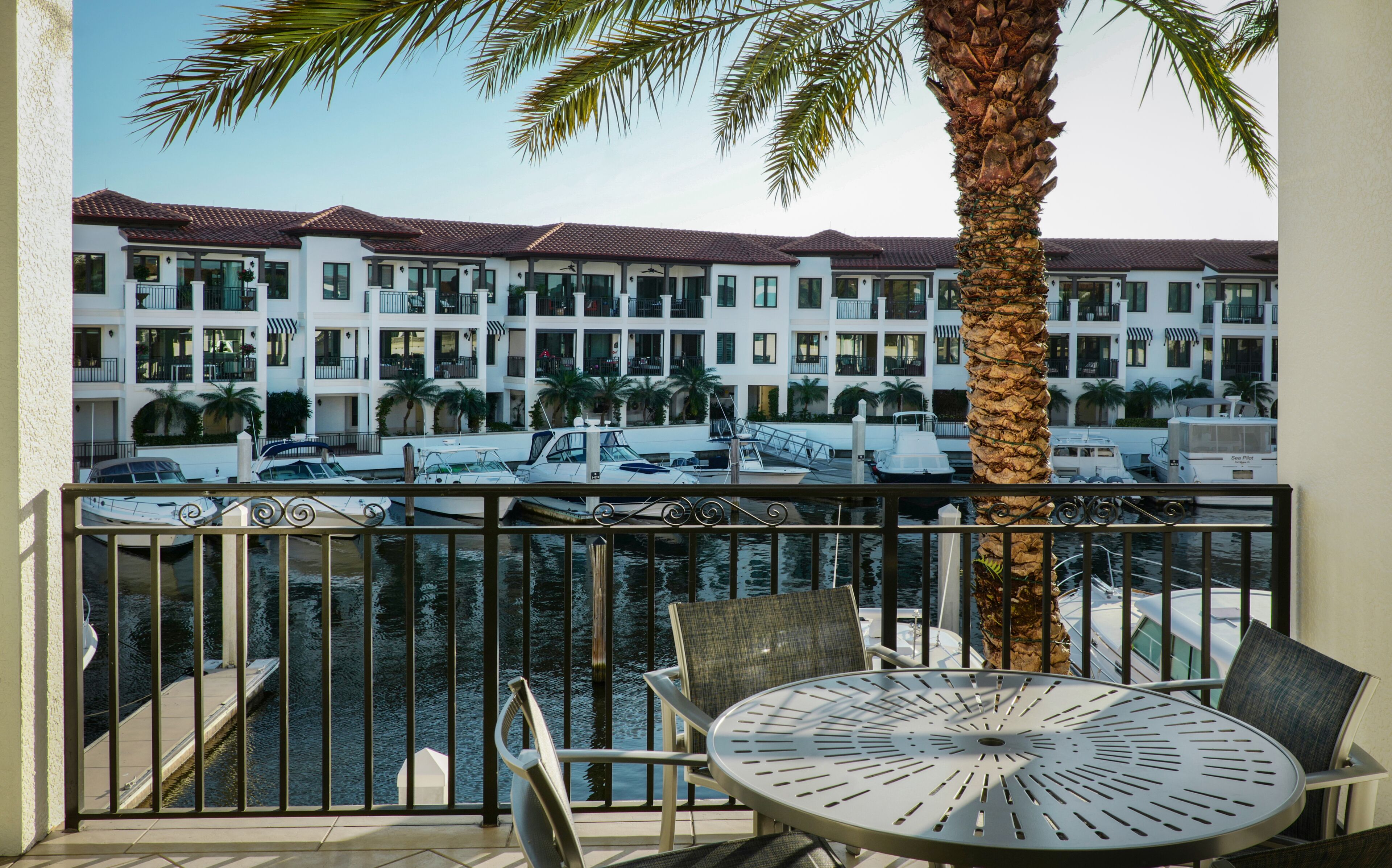 A balcony with a table and chairs, overlooking a marina with boats and a multi-story building with balconies.