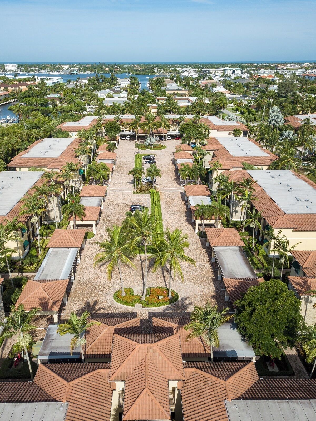 A resort with a central courtyard surrounded by rooms with red-tiled roofs, palm trees, and a marina in the background.