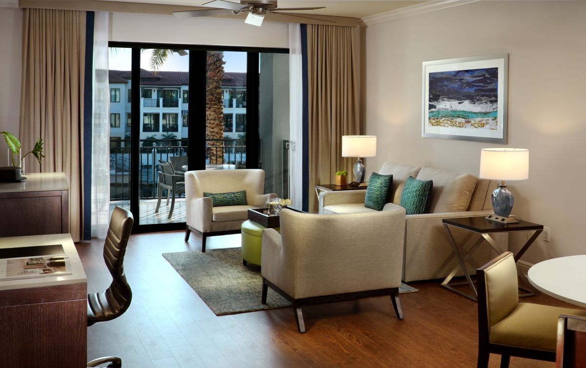 A hotel room with a balcony, a sofa set, a dining table, and a ceiling fan.