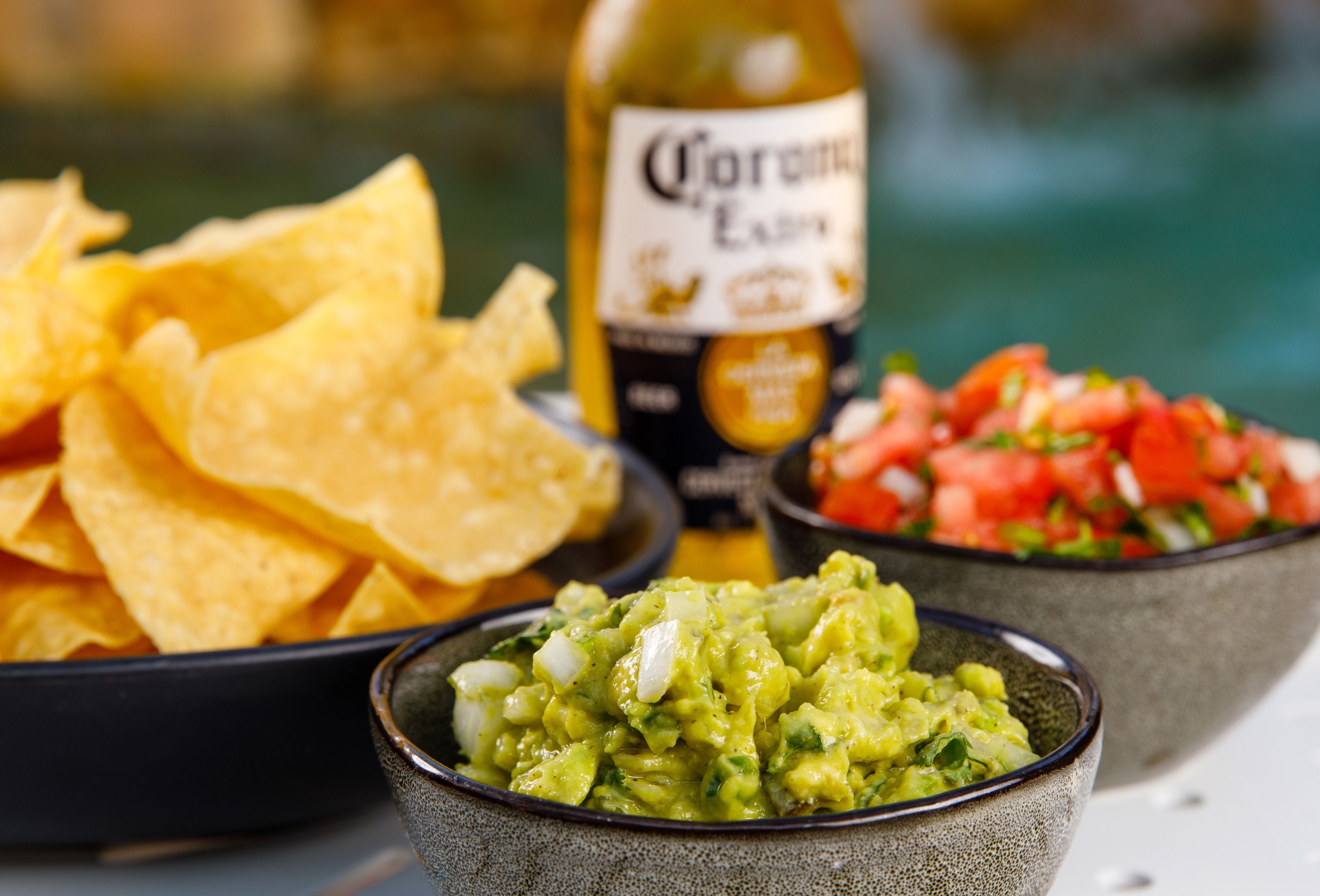 Un tazón de guacamole, un tazón de salsa y una botella de cerveza Corona.