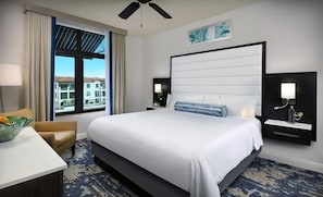 Una habitación de hotel con una cama grande, un escritorio, una silla, una ventana con vistas a edificios y un ventilador de techo.