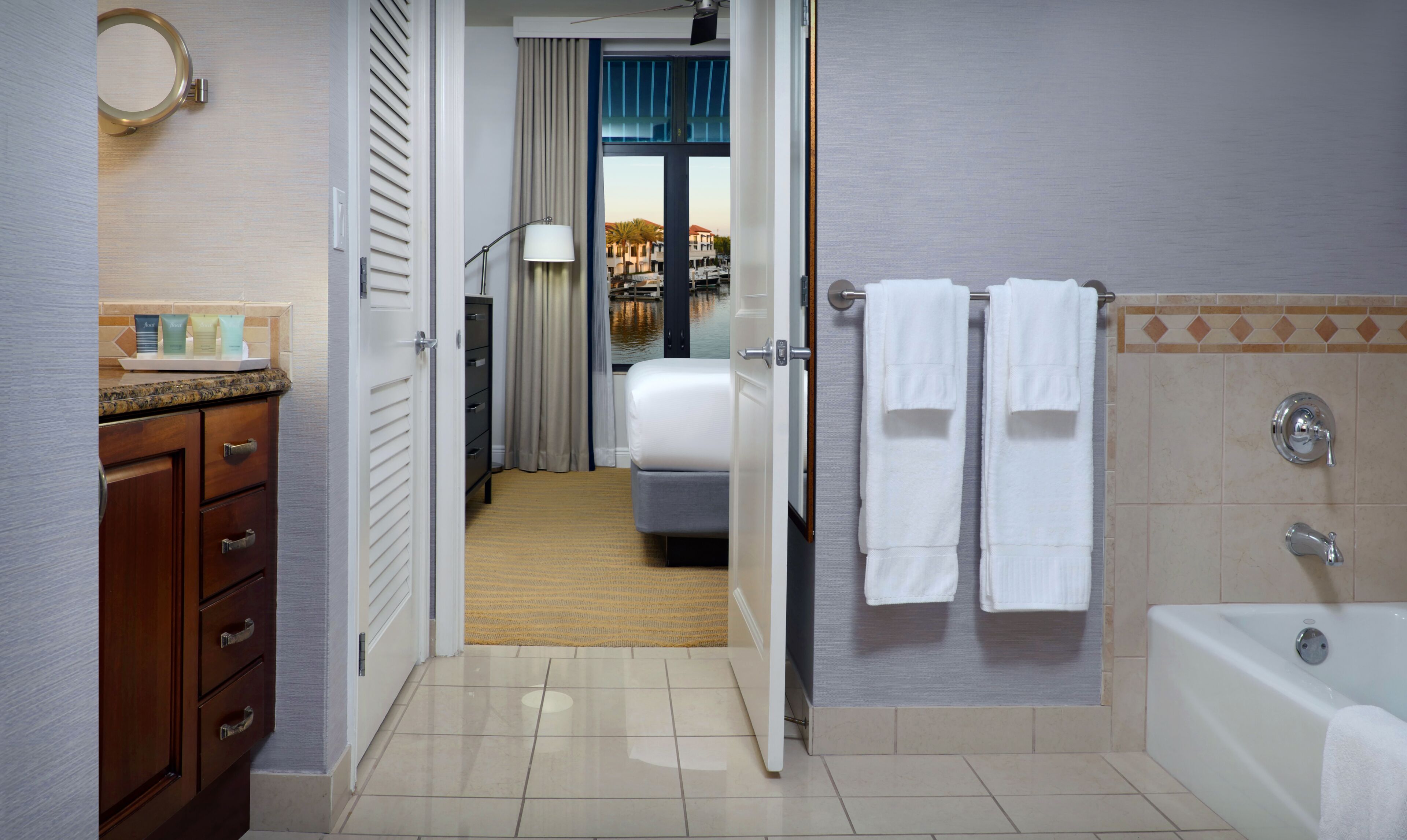 Un bagno d'albergo con una vasca, asciugamani, uno specchio e vista su un edificio attraverso una finestra.