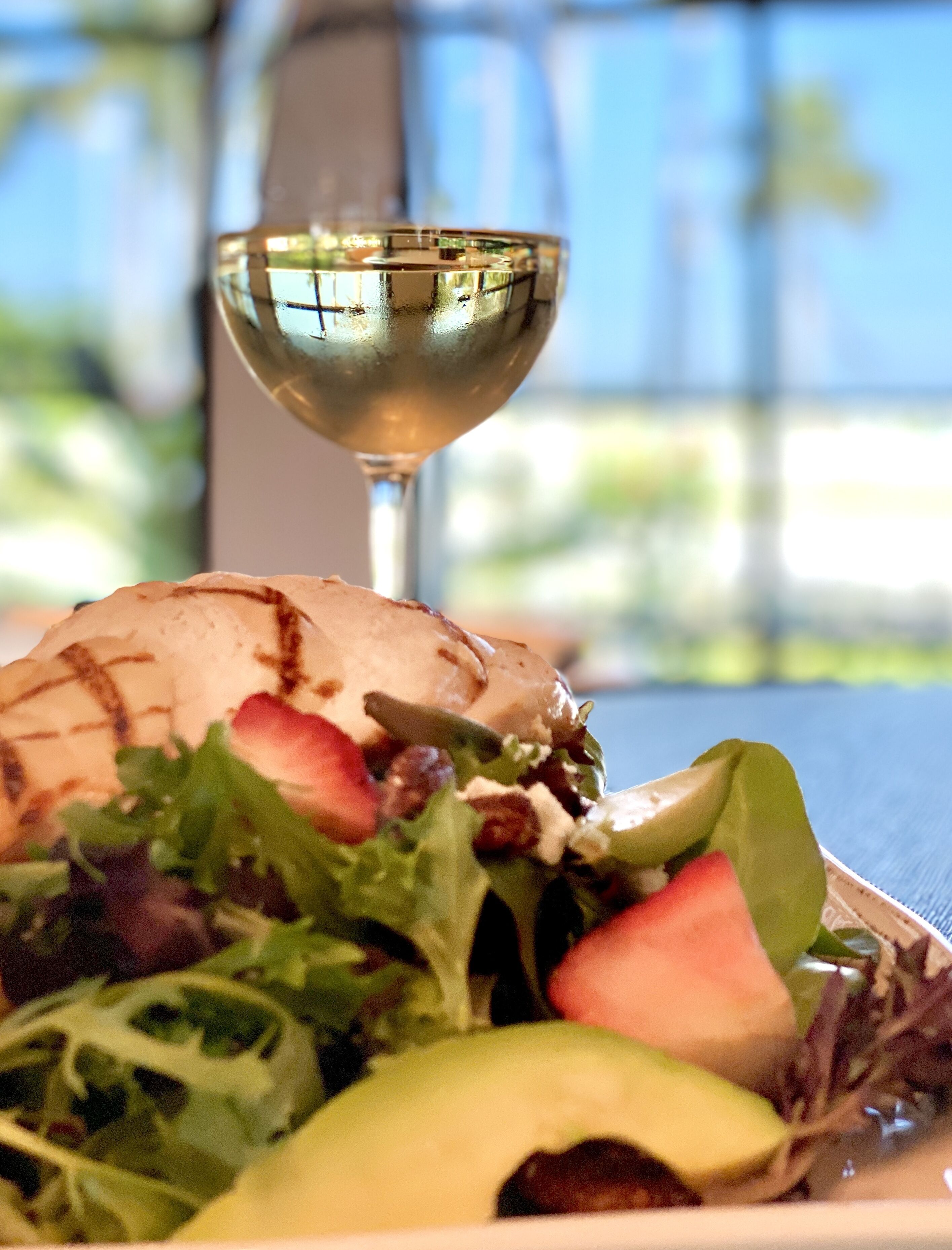 A plate with a salad, avocado, and a glass of white wine.