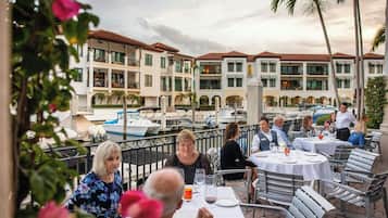 An outdoor dining area with tables and chairs, overlooking a marina with boats.