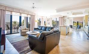 A spacious living area with a leather sofa, a coffee table, and a dining area with a kitchen in the background.