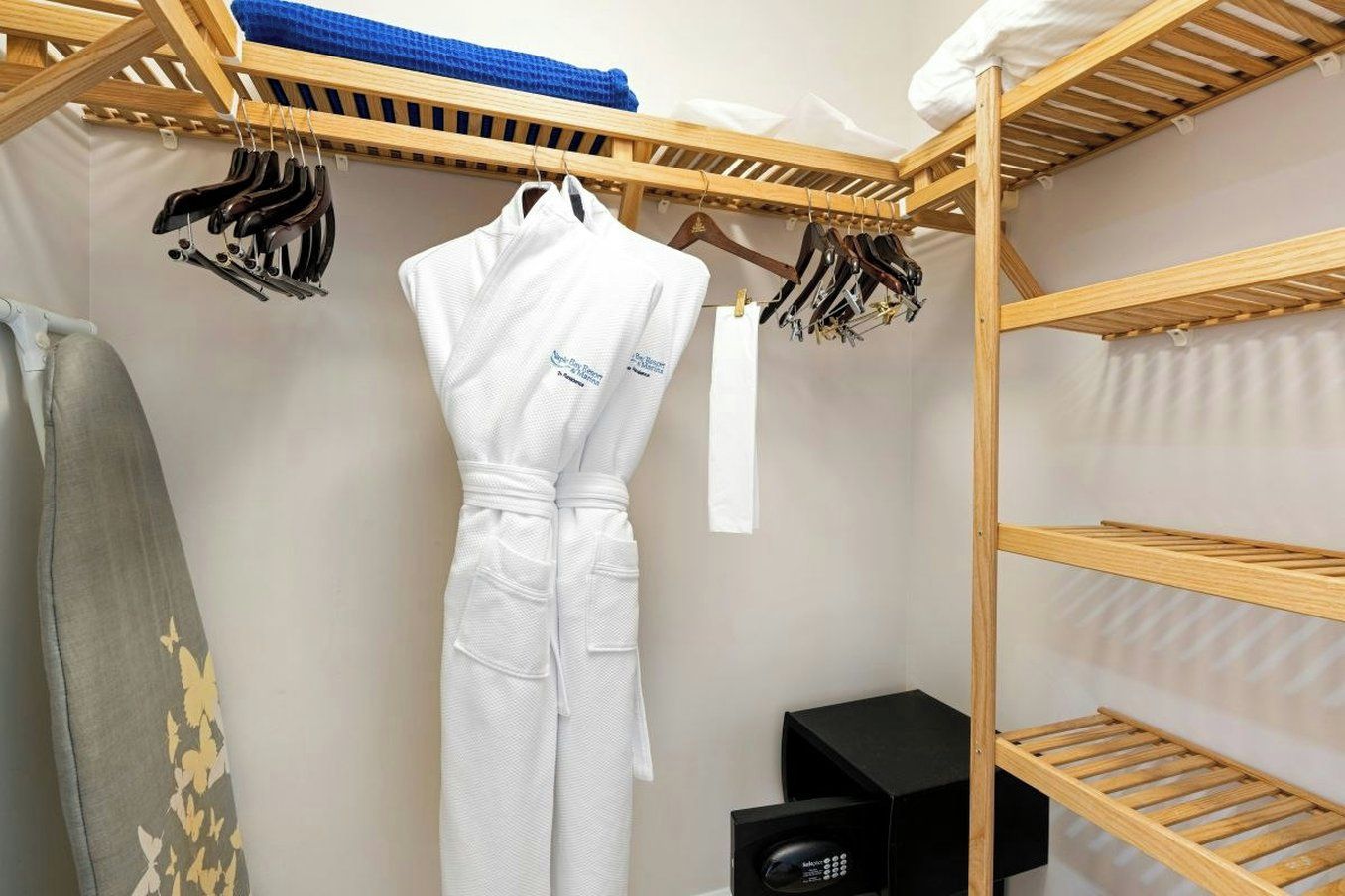 A hotel room with a wooden shelf unit, a white robe hanging, and a black speaker on the floor.
