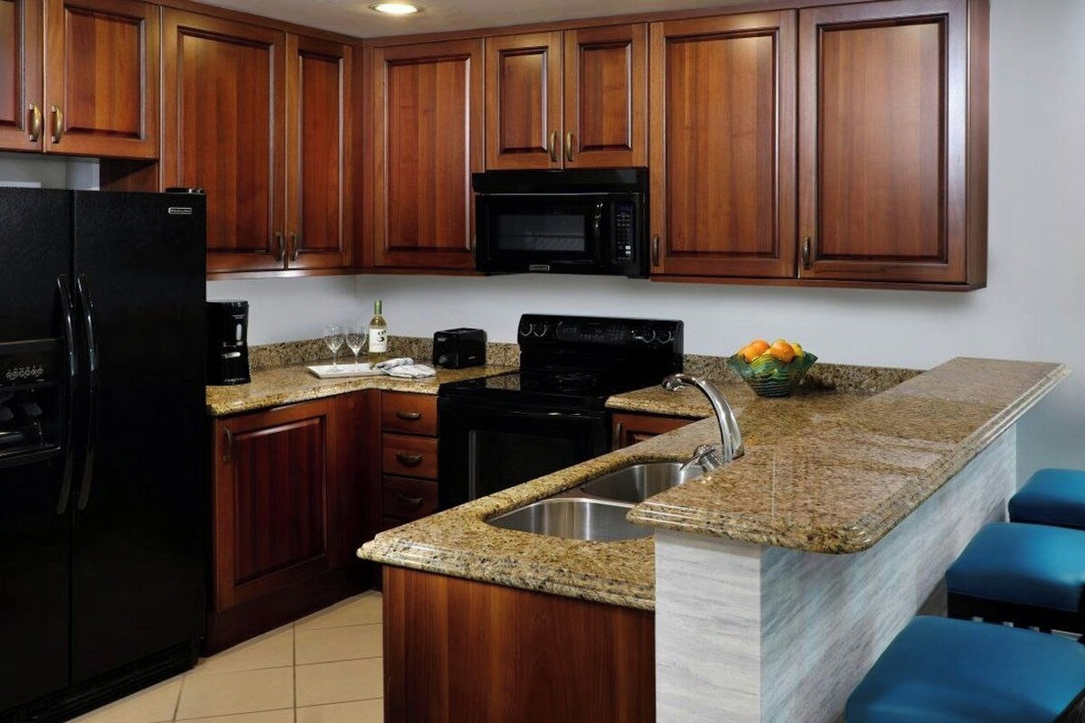 A kitchen with wooden cabinets, a black refrigerator, a microwave, a coffee maker, and a granite countertop.