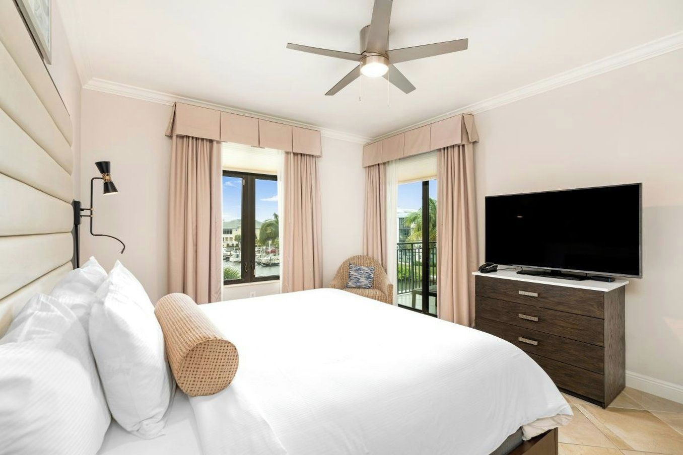Une chambre d’hôtel équipée d’un lit, d’une télévision, d’un ventilateur de plafond et offrant une vue sur l’extérieur.