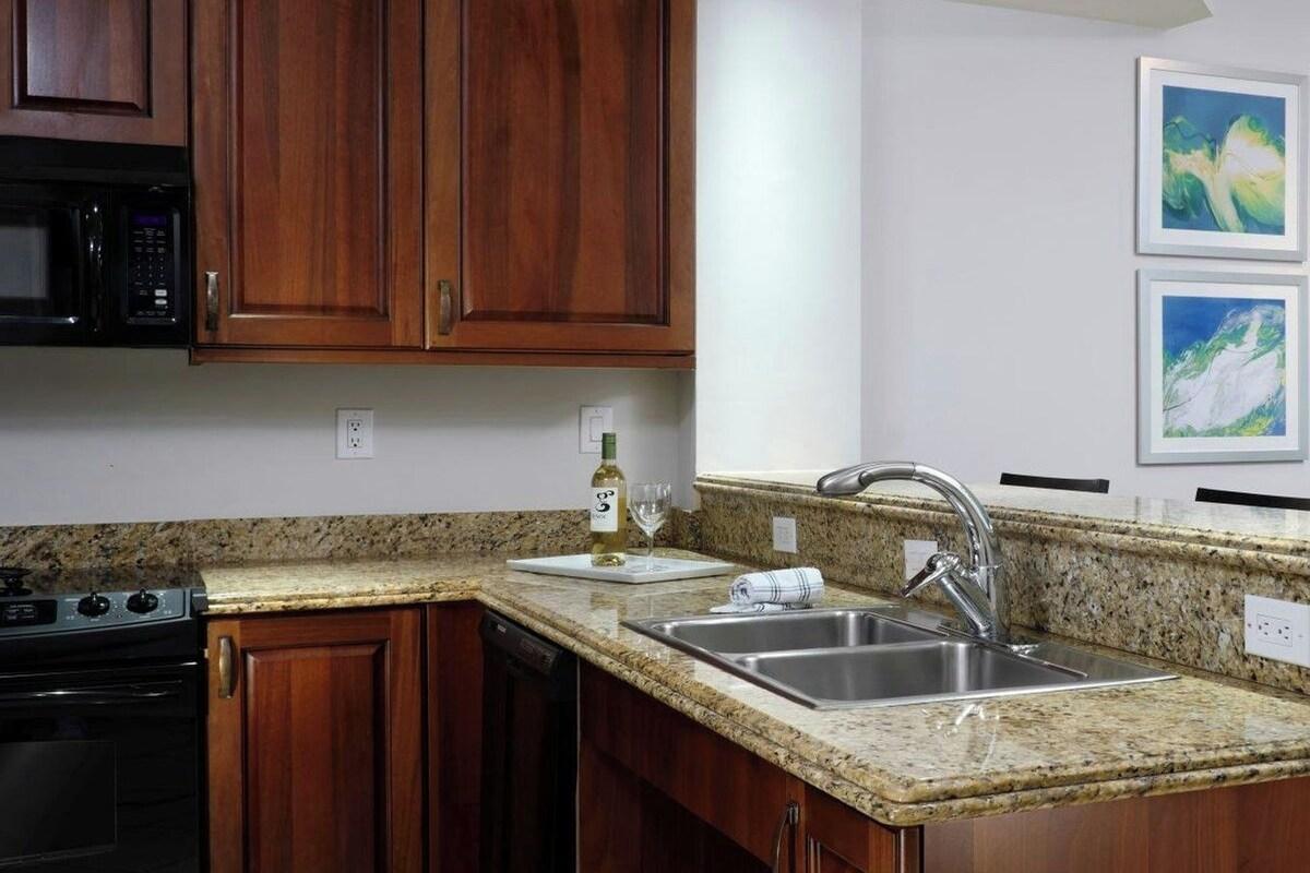 A kitchen with wooden cabinets, a granite countertop, a stainless steel sink, a microwave, and a dishwasher.