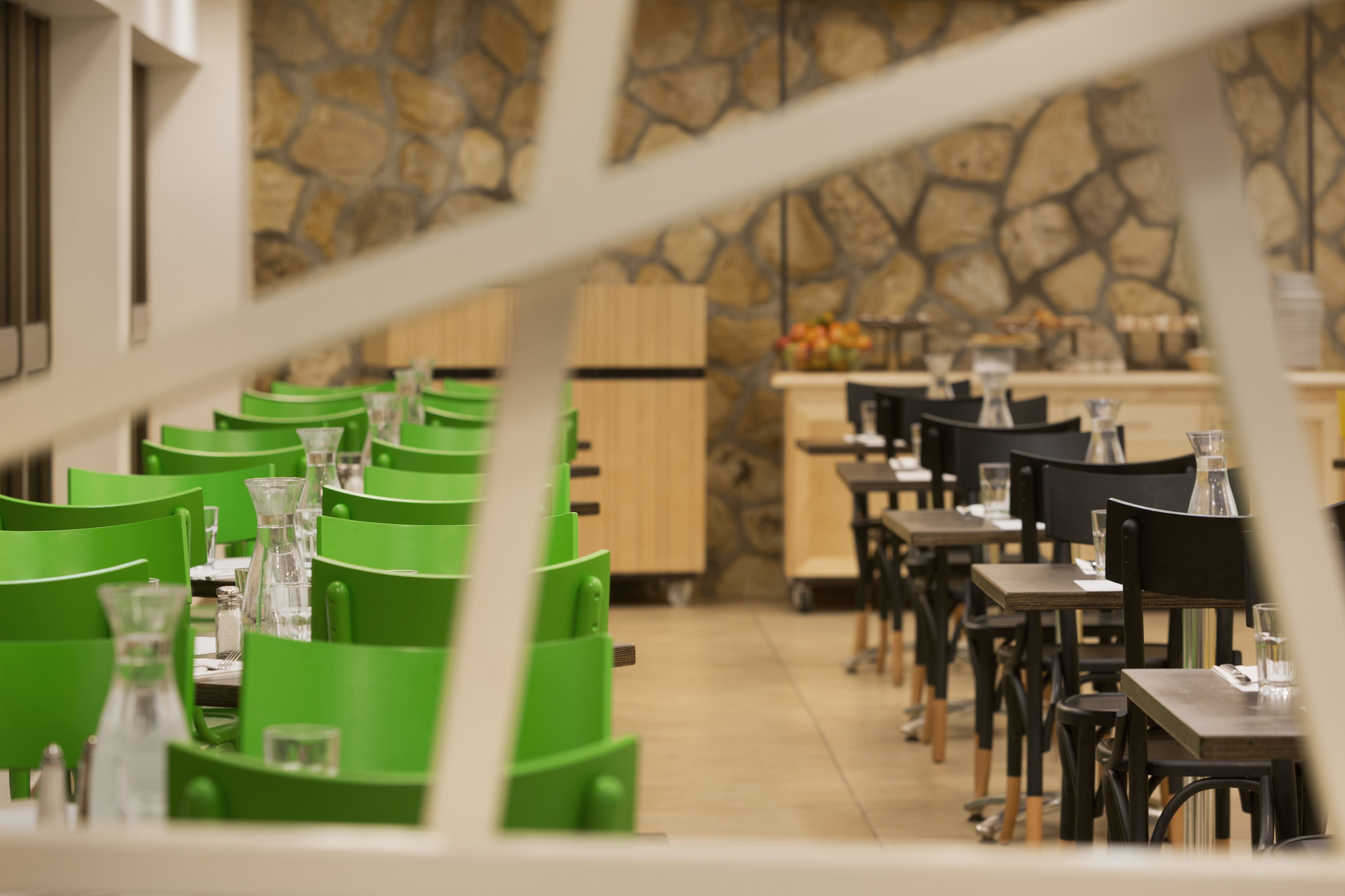 Un restaurante con sillas y mesas verdes, un fondo de pared de piedra y armarios de madera.