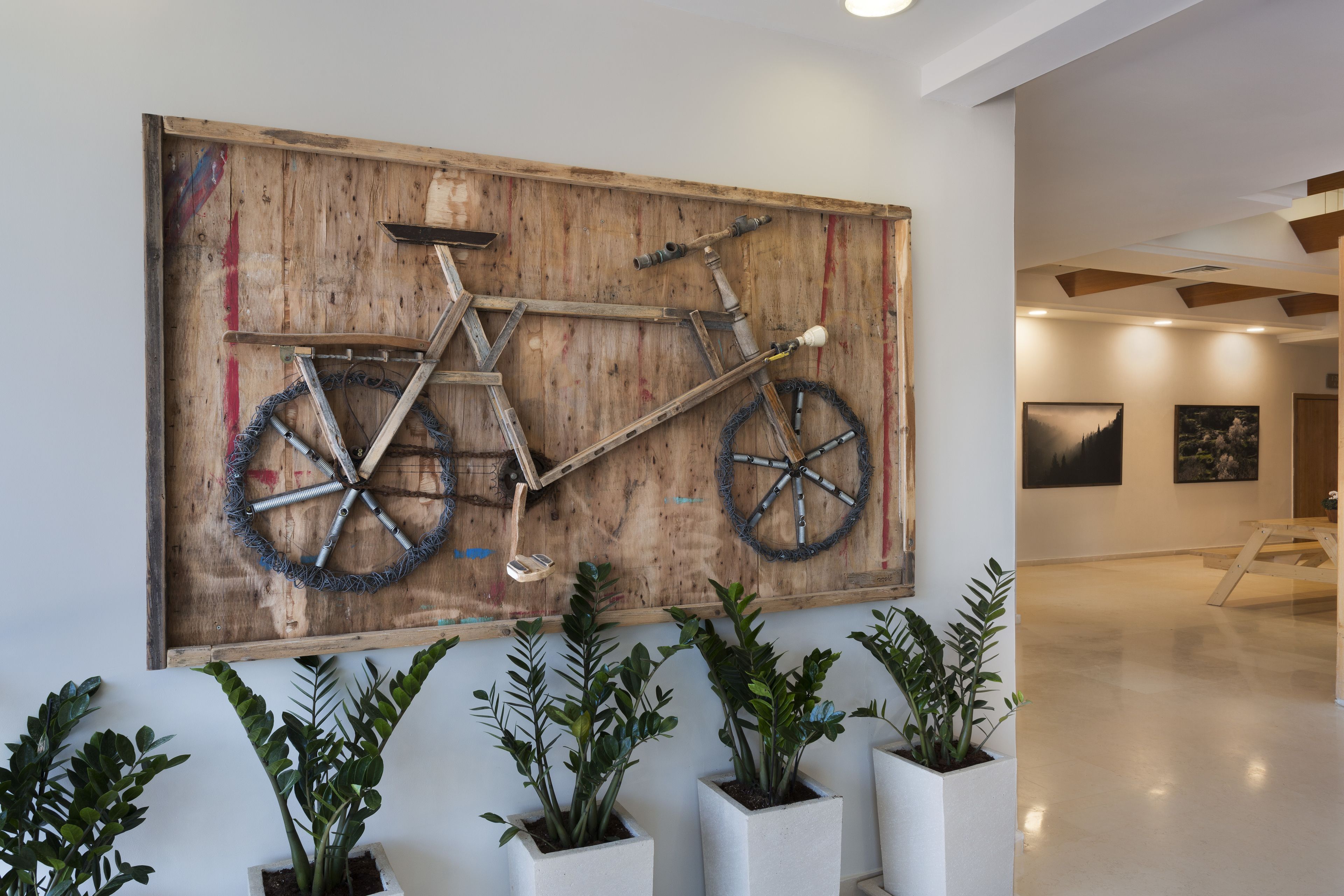 A large wooden artwork of a bicycle on a wall, surrounded by potted plants.