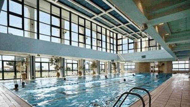 Une piscine intérieure avec des parois en verre transparent, un sol carrelé et un escalier en métal.