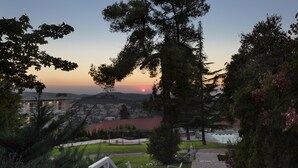Un jardin aménagé avec un sentier en pierre, un banc blanc et une vue sur le coucher de soleil au-dessus d’un quartier résidentiel.