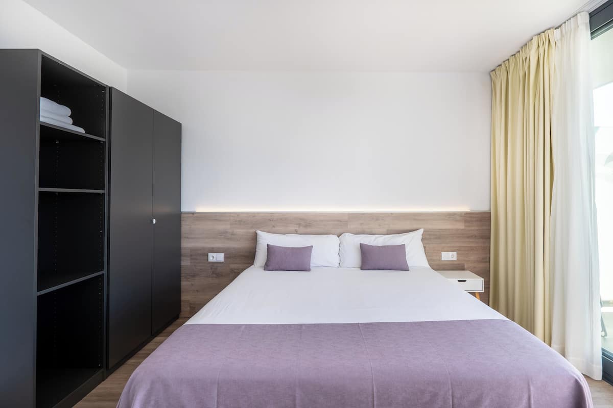 Habitación de hotel con cama, armario, mesita de noche y ventana con cortinas.