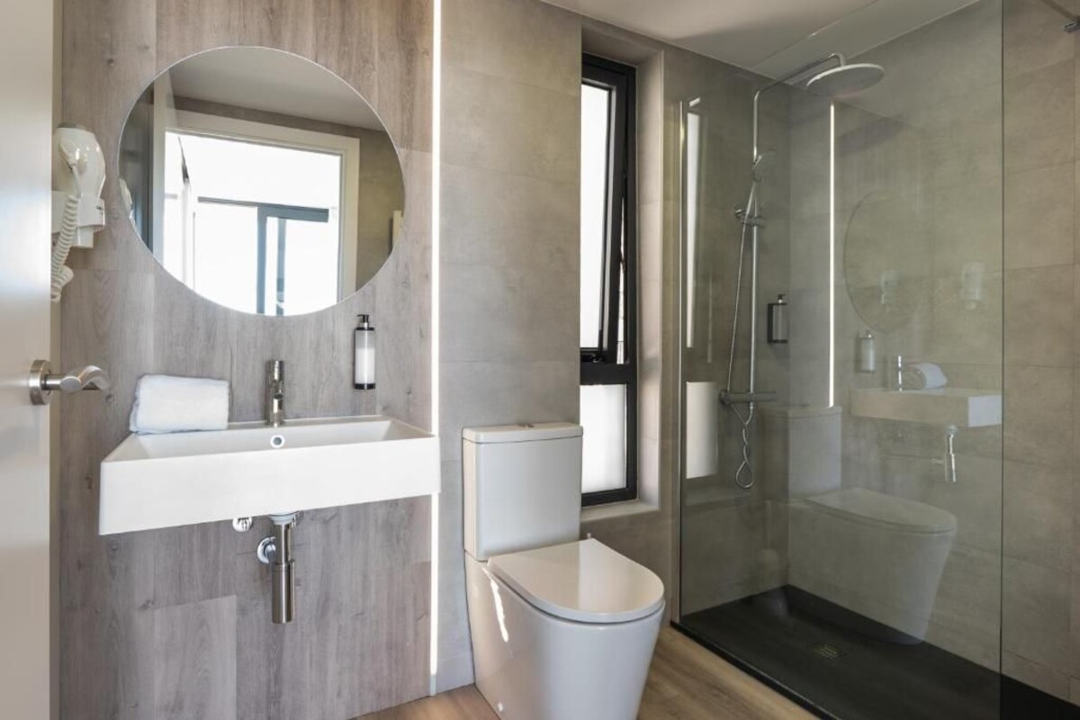 Une salle de bain moderne avec un meuble-lavabo en bois, des toilettes, une douche en verre et un grand miroir.