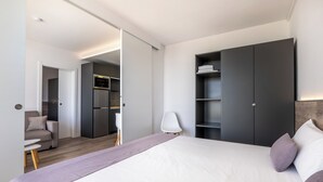 Habitación de hotel moderna con una cama grande, un armario, una zona de estar con una silla y una mesita.