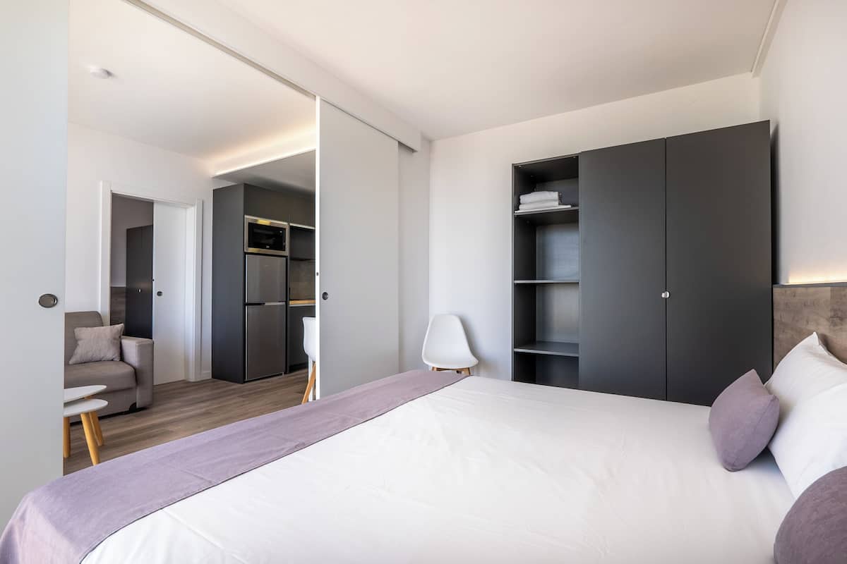 Habitación de hotel moderna con una cama grande, un armario, una zona de estar con una silla y una mesita.