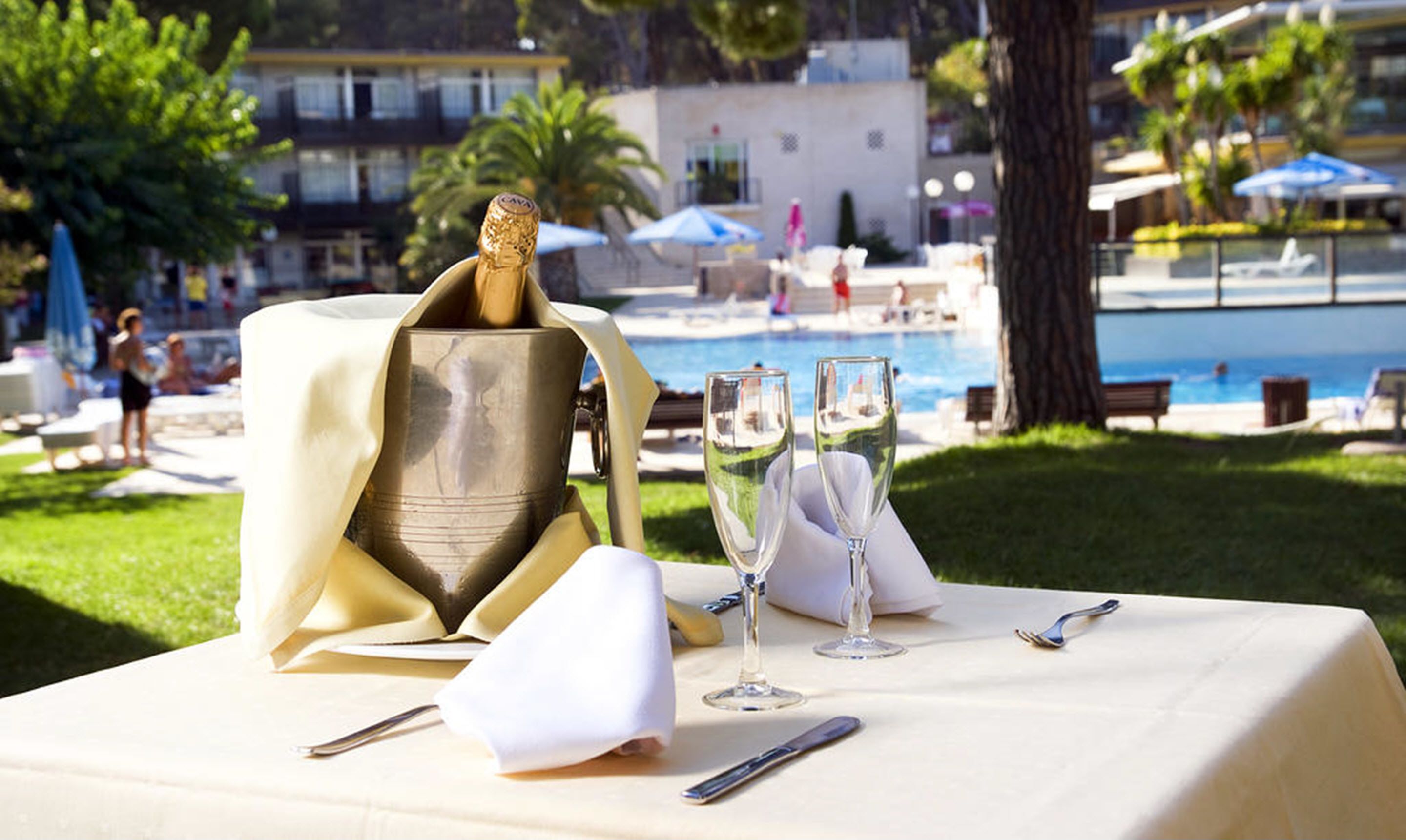 A table set for a meal with a bottle of champagne, two glasses, and cutlery.