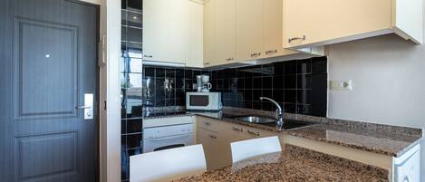 A modern kitchen with white cabinets, a granite countertop, a microwave, and a sink.