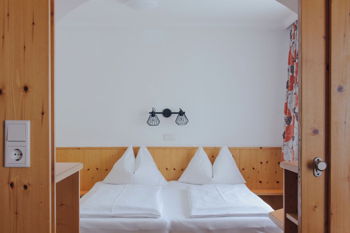 A wooden-framed bed with white bedding in a room with wooden walls and a sloped ceiling.