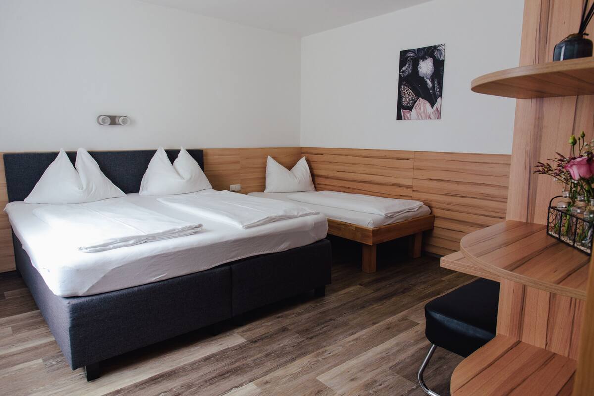 Una habitación de hotel moderna con una cama grande, una cama más pequeña, un banco de madera y un escritorio con una silla.