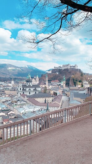 A panoramic view of a historic city with a prominent castle on a hill, surrounded by a mix of traditional and modern buildings. - Hotel Drei Kreuz (Salzburg)