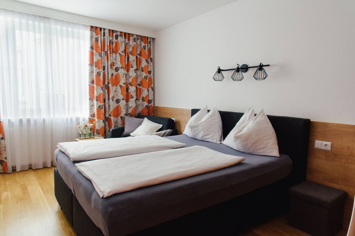 Una cama doble con ropa blanca, un cabecero de madera y una mesita de noche con un florero.