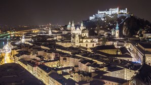 A historic cityscape at night with illuminated buildings, a prominent church, and a castle on a hill. - Hotel Drei Kreuz (Salzburg)