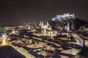 A historic cityscape at night with illuminated buildings, a prominent church, and a castle on a hill. - Hotel Drei Kreuz (Salzburg)