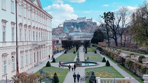 A formal garden with a central fountain, pathways, and a large building with classical architecture in the background. - Hotel Drei Kreuz (Salzburg)